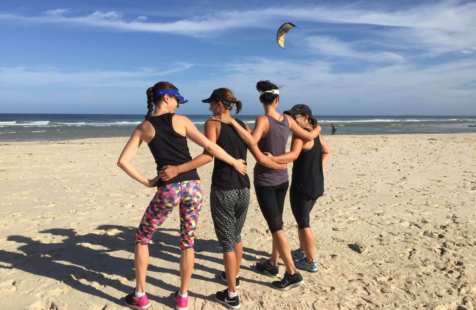 four women standing on a beach linking arms