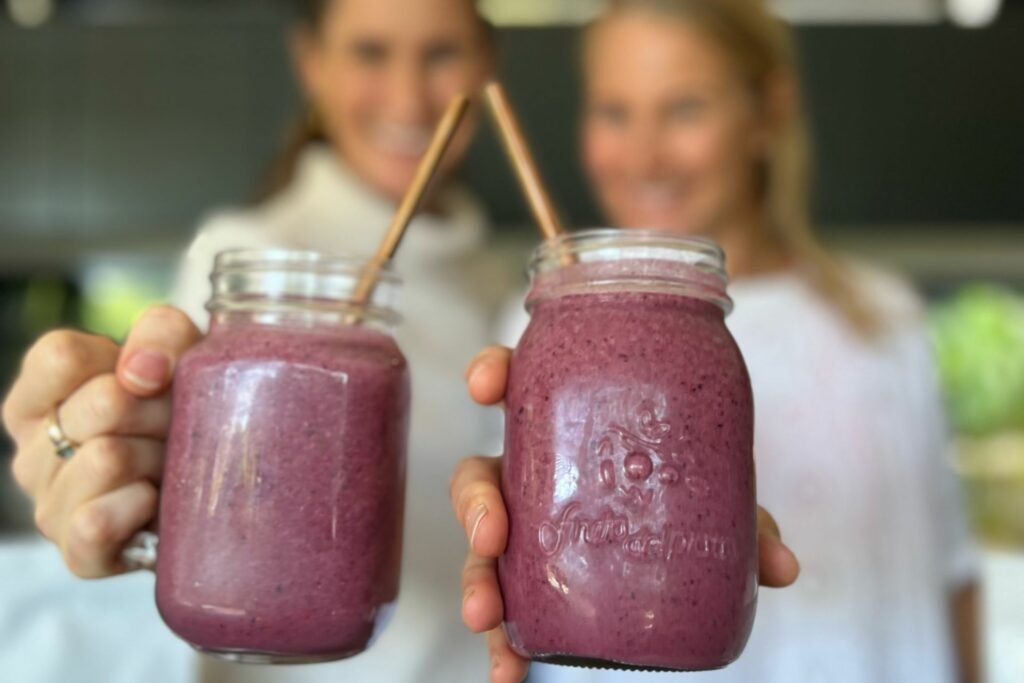 Anna and Em holding up a berry smoothie to the camera