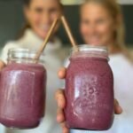 Anna and Em holding up a berry smoothie to the camera