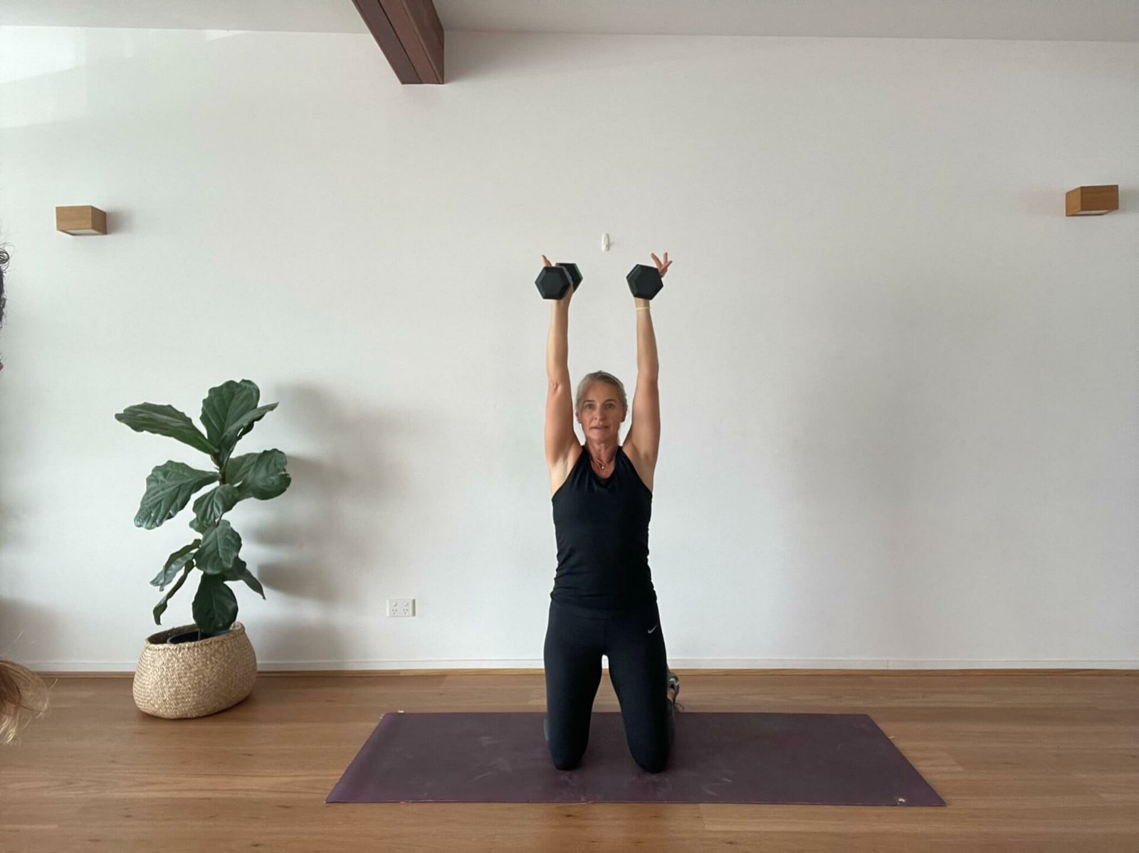 Anna in studio doing overhead press with dumbbells