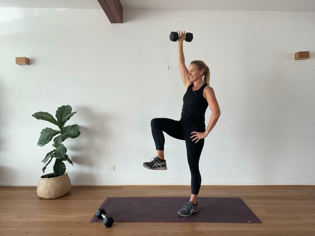 Anna in studio with high knee and single arm overhead press